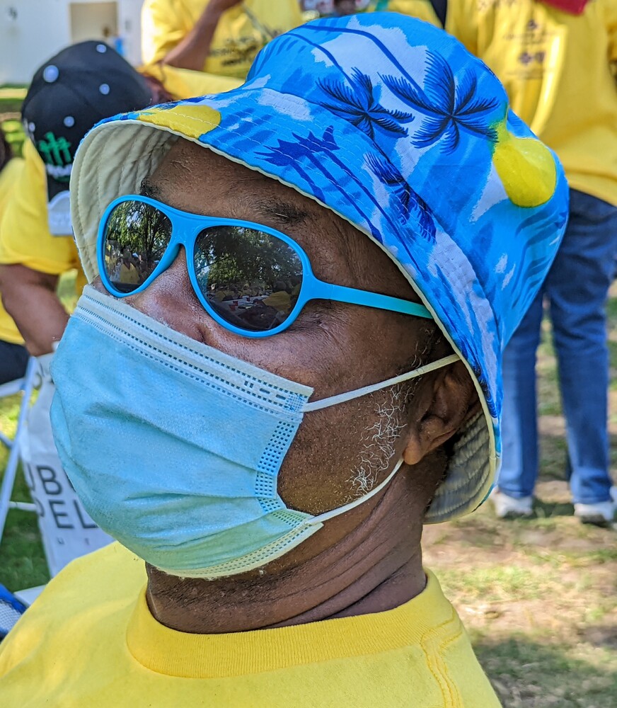 Older American attendee with mask, sunglasses, and a hat on.