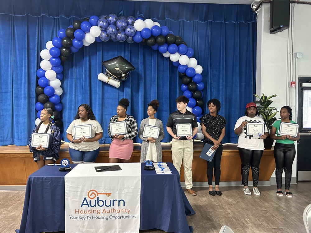 Auburn High School Graduates standing in front of stage holding certificates at the Auburn Housing Authority reception