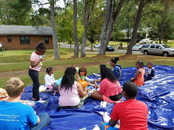 Youth on a large blue mat watching a Church of the Highlands staff member carving a pumpkin.