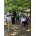 Juneteenth attendee speaking in a microphone outside as other attendees are sitting around listening.