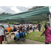 Individuals standing in line on the sidewalk near a parking lot waiting for their turn to pick from items on the display tables with free food and dry goods. 