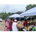 Individuals standing in front of vendor tents outside picking through items on display at the Farmers Market food tables.