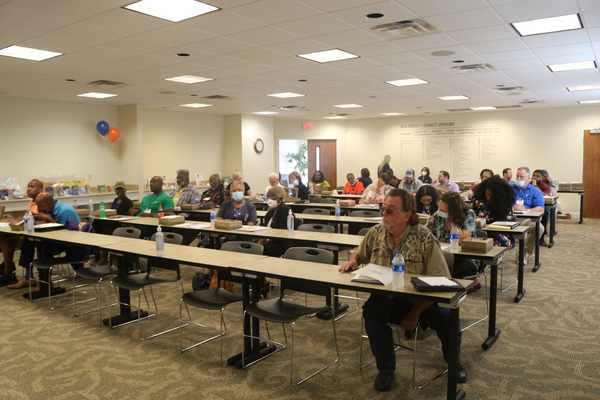 Landlord Symposium attendees are seated behind long rectangular tables looking towards the front of the room