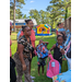 Youth are walking with new backpacks and snowcones with their families outside.  A inflatable house can be seen in the background