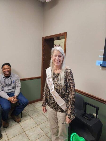 Sandra Sanders standing and smiling with retirement sash 
