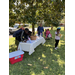 Cooler and table of snacks are outside on the lawn under tree, kids also are seen 